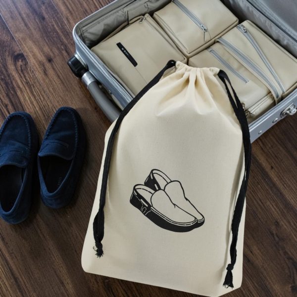 Sac à chaussures homme Été en coton écru ac à chaussures homme en coton écru imprimé mocassins, cordon noir, à côté d'une valise ouverte, MOONLAC chez Atelier Julac