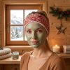 Bandeau de soins visage Noël rouge nordique porté masque chalet Femme avec un masque de soin vert portant un bandeau de soins visage Noël rouge motif nordique, devant la fenêtre d’une salle de bain de chalet, bandeau cousu main par Atelier Julac