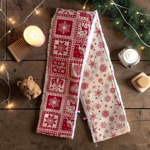 Deux bandeaux de soins visage Noël, un rouge nordique et un beige à flocons rouges, posés avec une bougie, un peigne en bois et des branches de sapin, cousus main par Atelier Julac