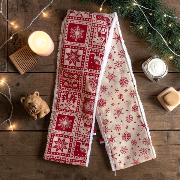 Bandeau de soins visage Noël rouge et beige chalet montagne Deux bandeaux de soins visage Noël, un rouge nordique et un beige à flocons rouges, posés avec une bougie, un peigne en bois et des branches de sapin, cousus main par Atelier Julac