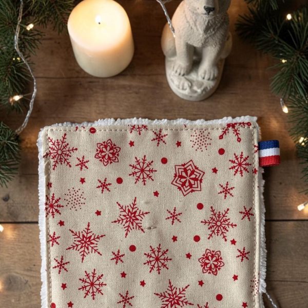 Coton démaquillant lavable Noël beige flocons de neige rouges Gros plan sur un coton démaquillant lavable Noël beige à flocons de neige rouges avec son étiquette bleu blanc rouge, posé près d’une bougie et de branches de sapin, cousu main par Atelier Julac