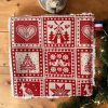 Coton démaquillant lavable Noël rouge motif nordique chalet cœur sapin Gros plan sur un coton démaquillant lavable Noël rouge à motif nordique avec cœur, chalet, sapins, oiseaux et étoile, avec son étiquette bleu blanc rouge, posé sur des branches de sapin, cousu main par Atelier Julac