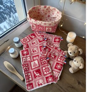Cotons démaquillants lavables Noël chalet montagne : lot de 10 cotons rouges à motif nordique avec leur panière beige à flocons rouges, posés avec pots de soin et oursons, cousus main par Atelier Julac