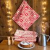 Essuie-tout lavables motifs Noël montagne cuisine chalet Essuie-tout lavables Noël rouges et beiges accrochés et empilés sur une étagère en bois avec guirlande lumineuse, gâteau et théière, cousus main par Atelier Julac