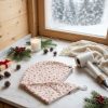 Serviette cheveux bambou Noël beige flocons de neige chalet Serviette cheveux en bambou Noël beige à flocons de neige rouges, posée sur un plan de salle de bain en marbre avec bougie, branches de sapin et sèche-cheveux, devant une fenêtre enneigée, cousue main par Atelier Julac
