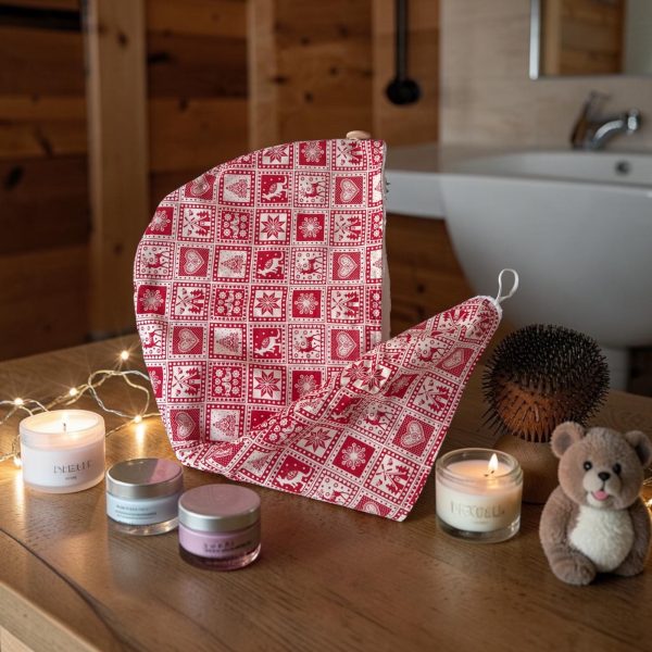 Serviette cheveux bambou Noël rouge nordique bougies salle de bain chalet Serviette cheveux en bambou Noël rouge motif nordique posée sur un plan en bois avec bougies, pots de soin et ourson, devant une baignoire de chalet, cousue main par Atelier Julac