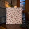 Serviette pour invités Noël montagne flocons de neige rouges Panière de serviettes pour invités Noël montagne, serviette en coton imprimé flocons de neige rouges sur fond écru, posée près de bougies et de branches de sapin - Atelier Julac